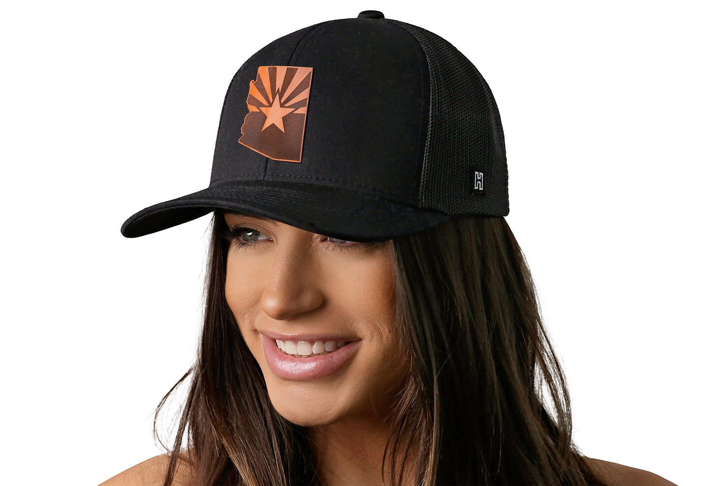 Black trucker hat worn by a female model viewed from the left side and features a Arizona Flag Leather Cut to Shape Flag Patch displayed on the front panel. The hat has a classic mesh back design and a curved structured bill