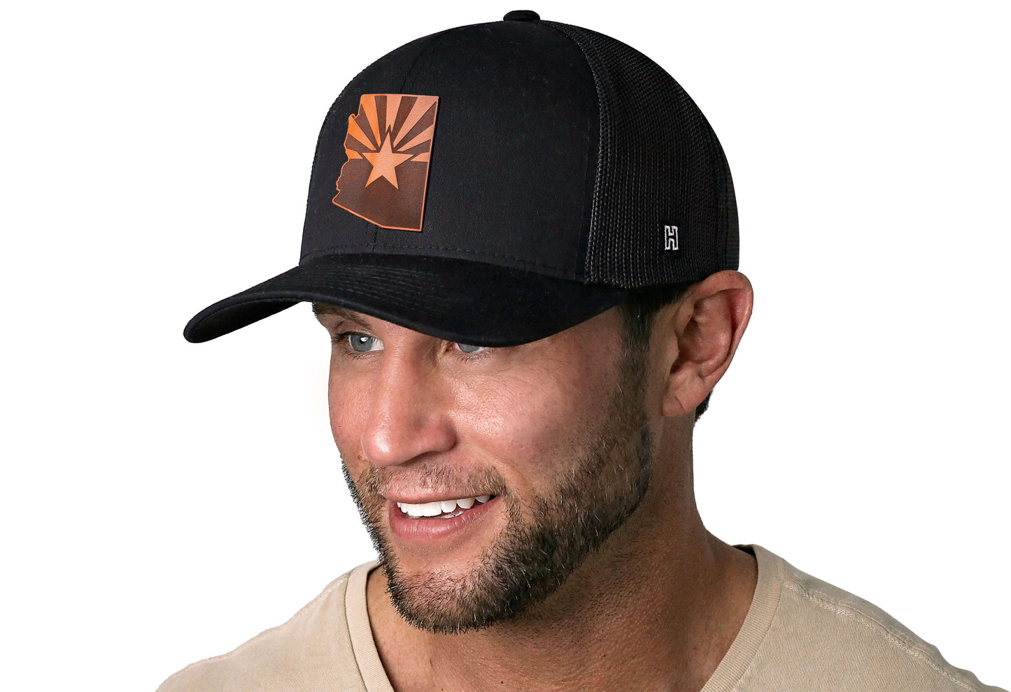 Black trucker hat worn by a male model viewed from the left side and features a Arizona Flag Leather Cut to Shape Flag Patch displayed on the front panel. The hat has a classic mesh back design and a curved structured bill
