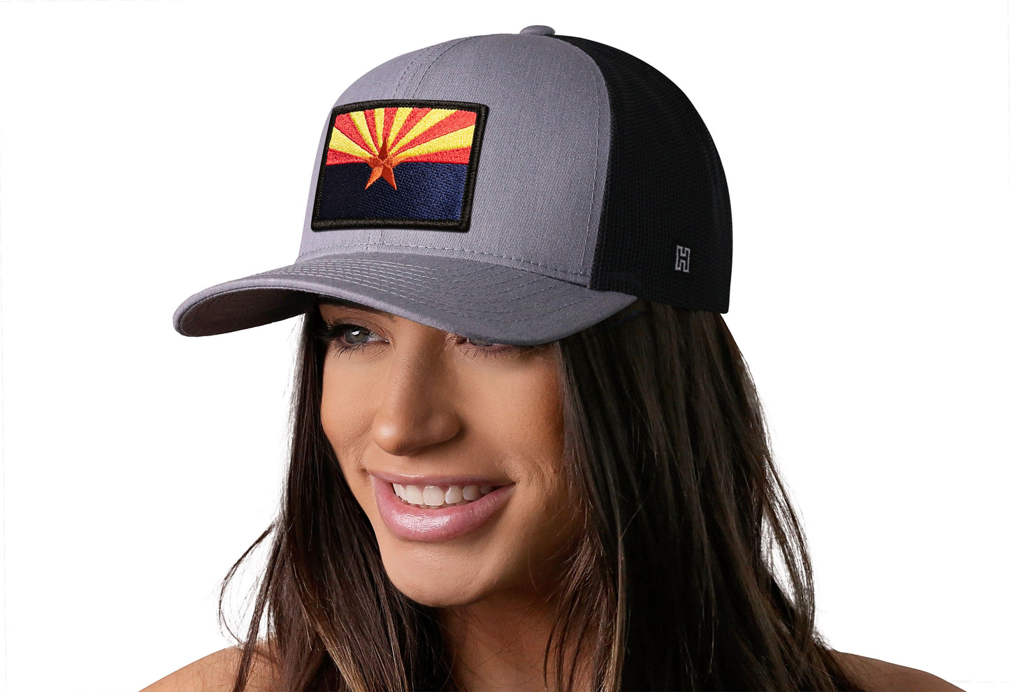Gray-Black trucker hat worn by a female model viewed from the left side and features a Arizona Flag Embroidered Rectangle Patch displayed on the front panel. The hat has a classic mesh back design and a curved structured bill