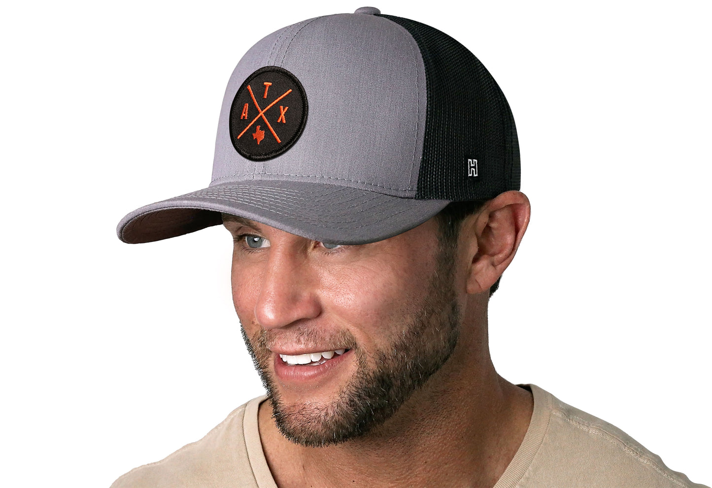 Gray-Black trucker hat worn by a male model viewed from the left side and features a Austin Gray-Orange ATX Embroidered X Patch displayed on the front panel. The hat has a classic mesh back design and a curved structured bill