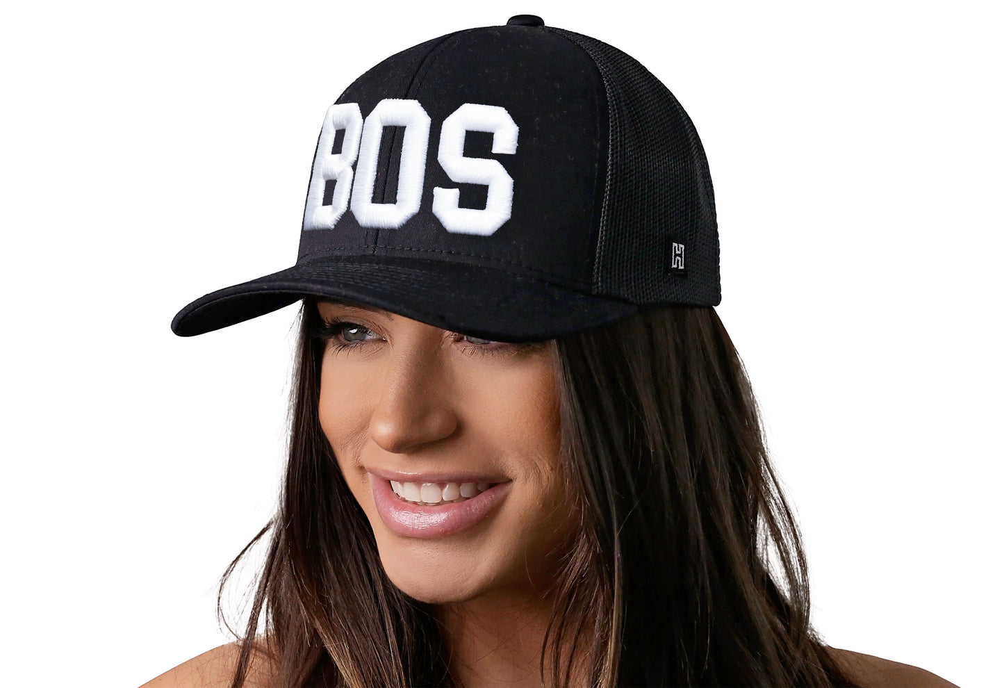 Black trucker hat worn by a female model viewed from the left side and features a BOS 3-D Puff Direct Embroidery displayed on the front panel. The hat has a classic mesh back design and a curved structured bill