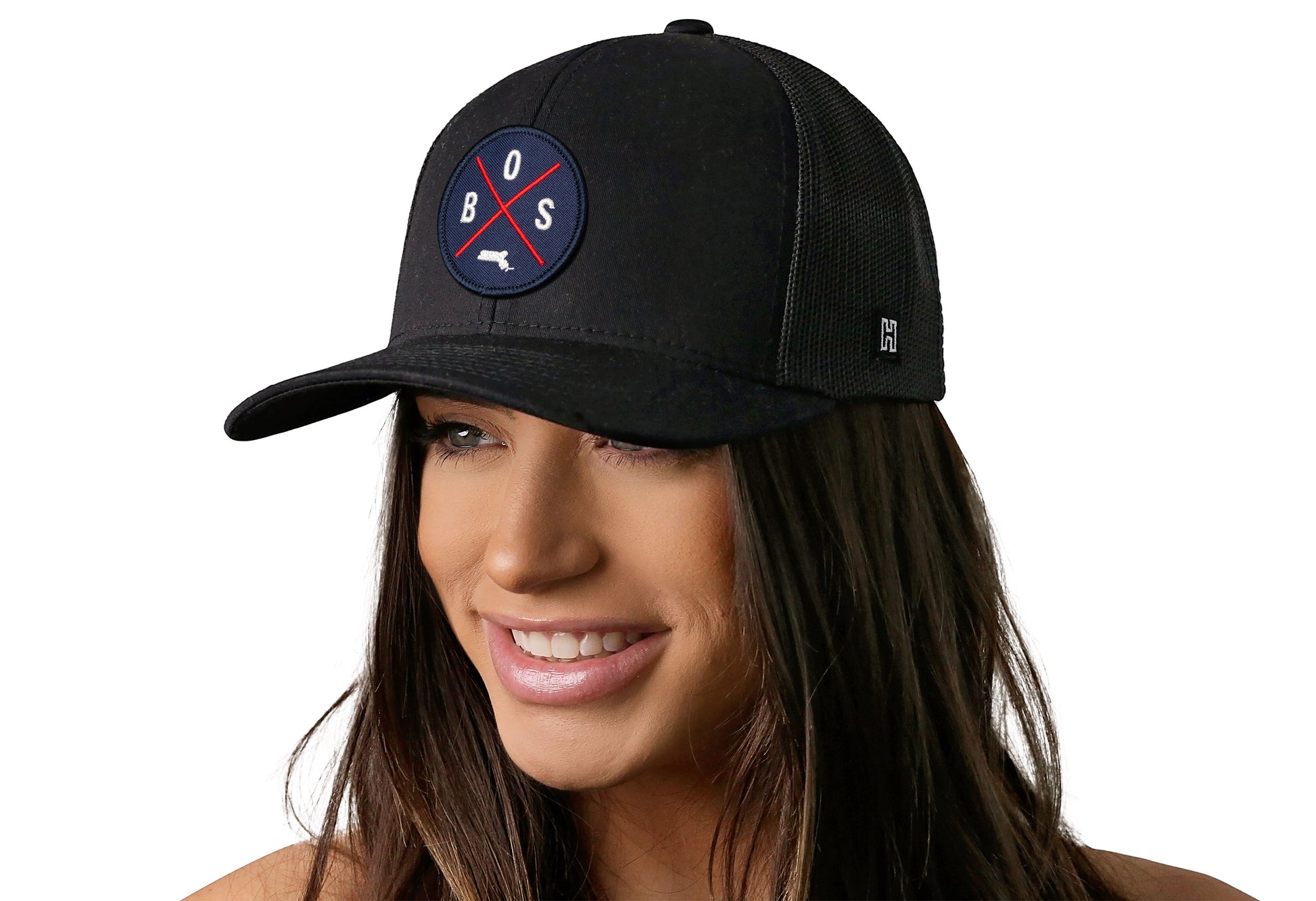 Black trucker hat worn by a female model viewed from the left side and features a Boston BOS X Red & Navy Embroidered Circle Patch displayed on the front panel. The hat has a classic mesh back design and a curved structured bill