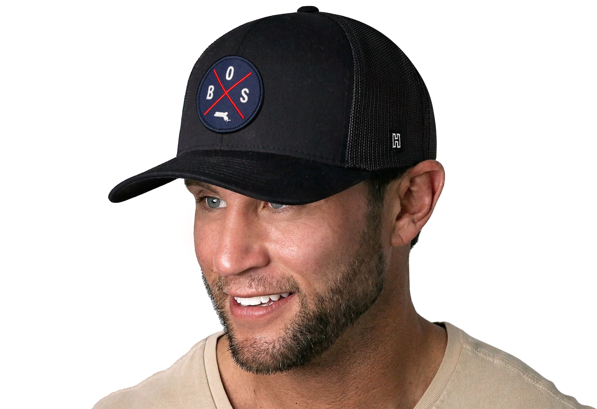 Black trucker hat worn by a male model viewed from the left side and features a Boston BOS X Red & Navy Embroidered Circle Patch displayed on the front panel. The hat has a classic mesh back design and a curved structured bill