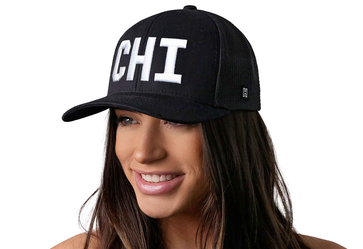 Black trucker hat worn by a female model viewed from the left side and features a White "CHI" Puff Embroidery Block displayed on the front panel. The hat has a classic mesh back design and a curved structured bill