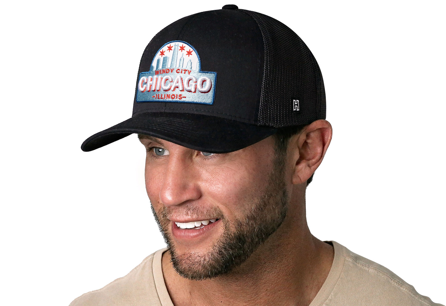 Black trucker hat worn by a male model viewed from the left side and features a Chicago Cityscape Embroidered Patch displayed on the front panel. The hat has a classic mesh back design and a curved structured bill