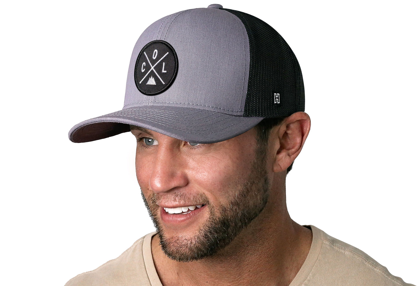 Gray-Black trucker hat worn by a male model viewed from the left side and features a Colorado COL X Embroidered Circle Patch displayed on the front panel. The hat has a classic mesh back design and a curved structured bill