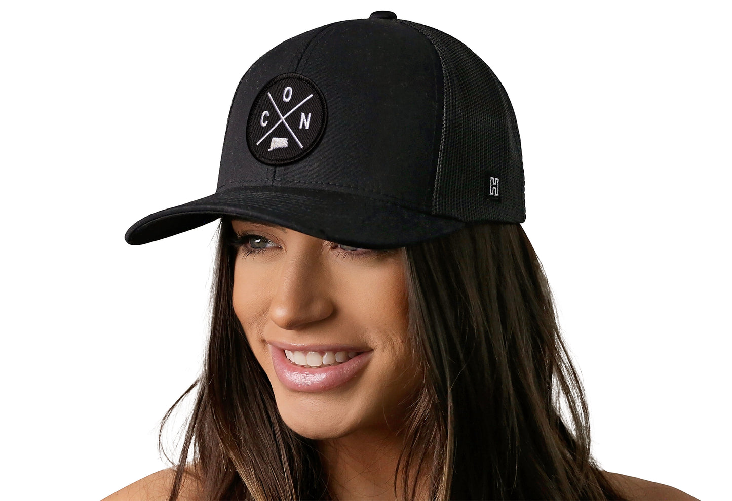 Black trucker hat worn by a female model viewed from the left side and features a Connecticut CON X Embroidered Circle Patch displayed on the front panel. The hat has a classic mesh back design and a curved structured bill