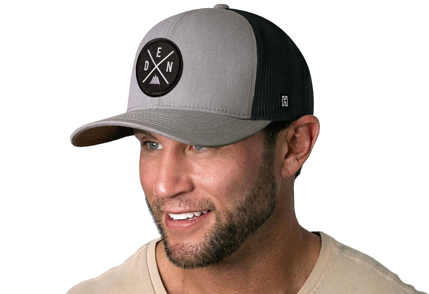 Gray-Black trucker hat worn by a male model viewed from the left side and features a Denver DEN X Embroidered Circle Patch displayed on the front panel. The hat has a classic mesh back design and a curved structured bill