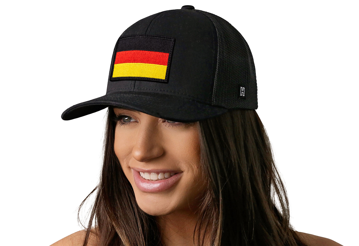Black trucker hat worn by a female model viewed from the left side and features a German Flag Embroidered Rectangle Patch displayed on the front panel. The hat has a classic mesh back design and a curved structured bill