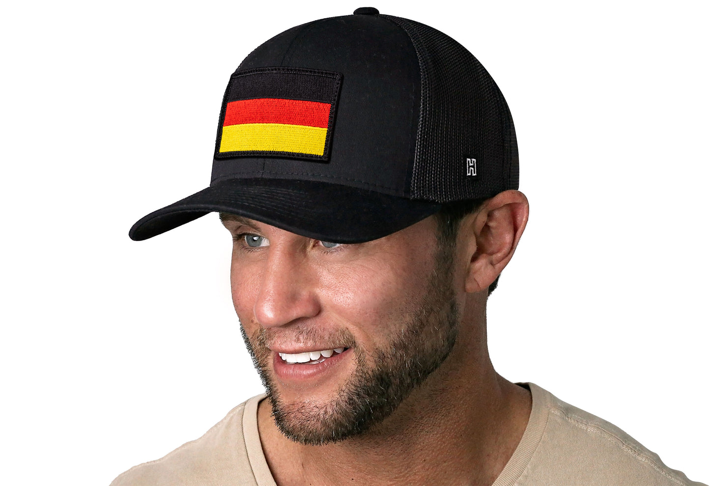 Black trucker hat worn by a male model viewed from the left side and features a German Flag Embroidered Rectangle Patch displayed on the front panel. The hat has a classic mesh back design and a curved structured bill