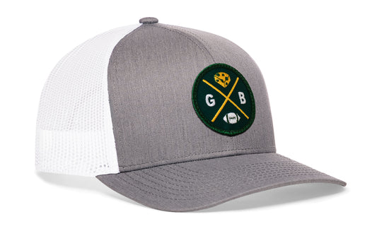 gray-white trucker hat viewed from the right side, showcasing a GB Football embroidered X patch in dark green and gold prominently displayed on the front
