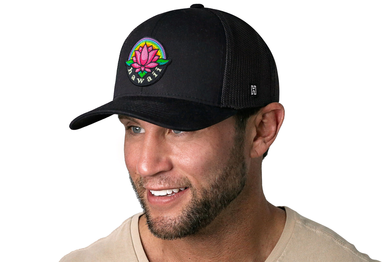 Black trucker hat worn by a male model viewed from the left side and features a Hawaii Flower Embroidered Patch displayed on the front panel. The hat has a classic mesh back design and a curved structured bill