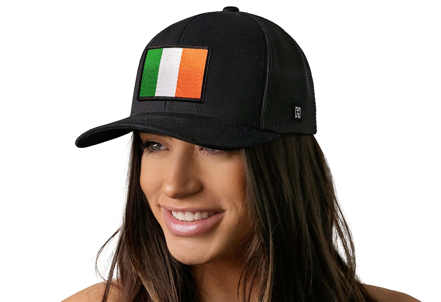 Black trucker hat worn by a female model viewed from the left side and features a Ireland Flag Embroidered Rectangle Patch displayed on the front panel. The hat has a classic mesh back design and a curved structured bill