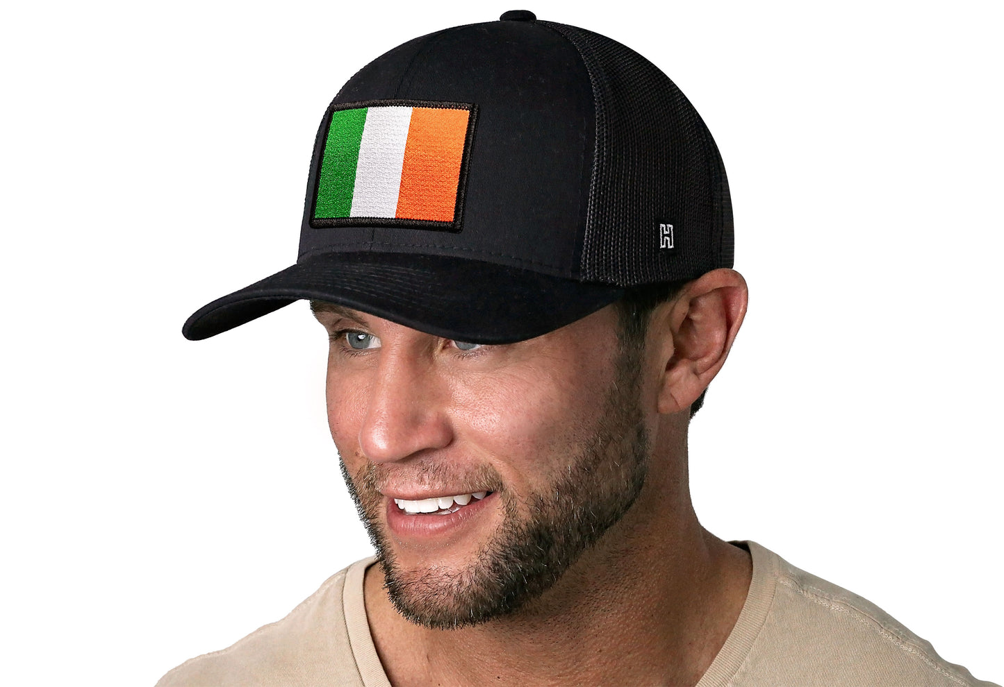 Black trucker hat worn by a male model viewed from the left side and features a Ireland Flag Embroidered Rectangle Patch displayed on the front panel. The hat has a classic mesh back design and a curved structured bill