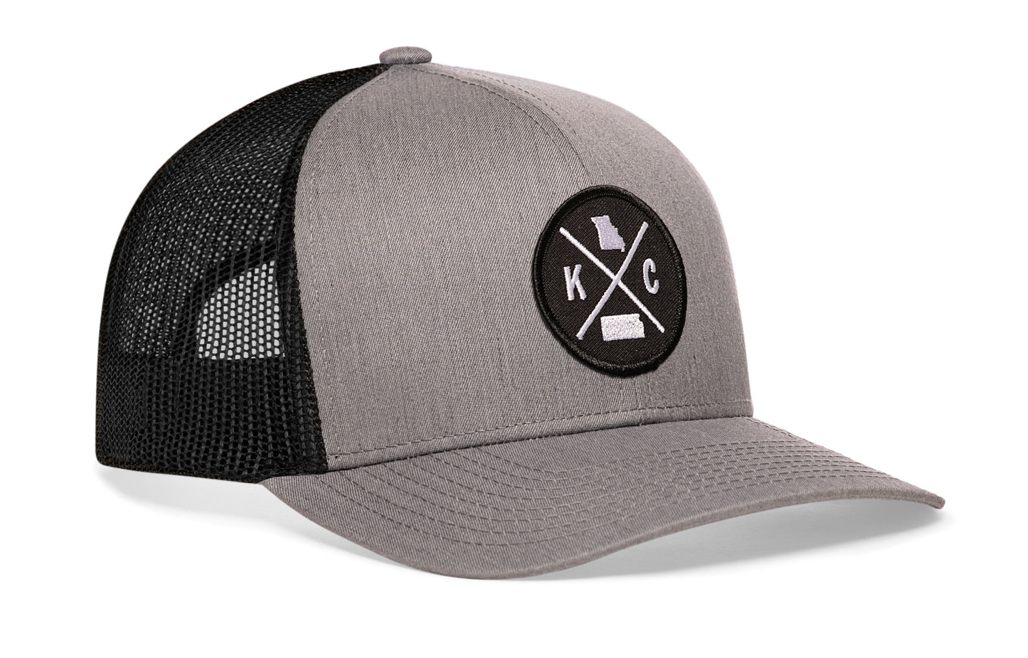 Gray-Black trucker hat viewed from the right side, showcasing a Kansas City KC X Embroidered Circle Patch prominently displayed on the front