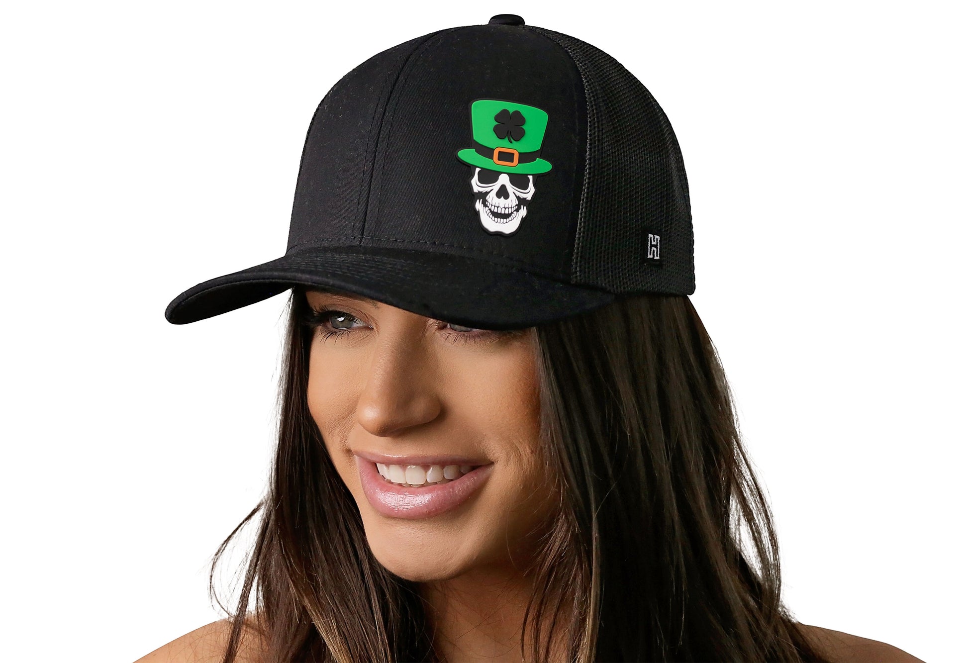 Black trucker hat worn by a female model viewed from the left side and features a Kiss me I'm Irish Puff Embroidered Circle Patch displayed on the front panel. The hat has a classic mesh back design and a curved structured bill