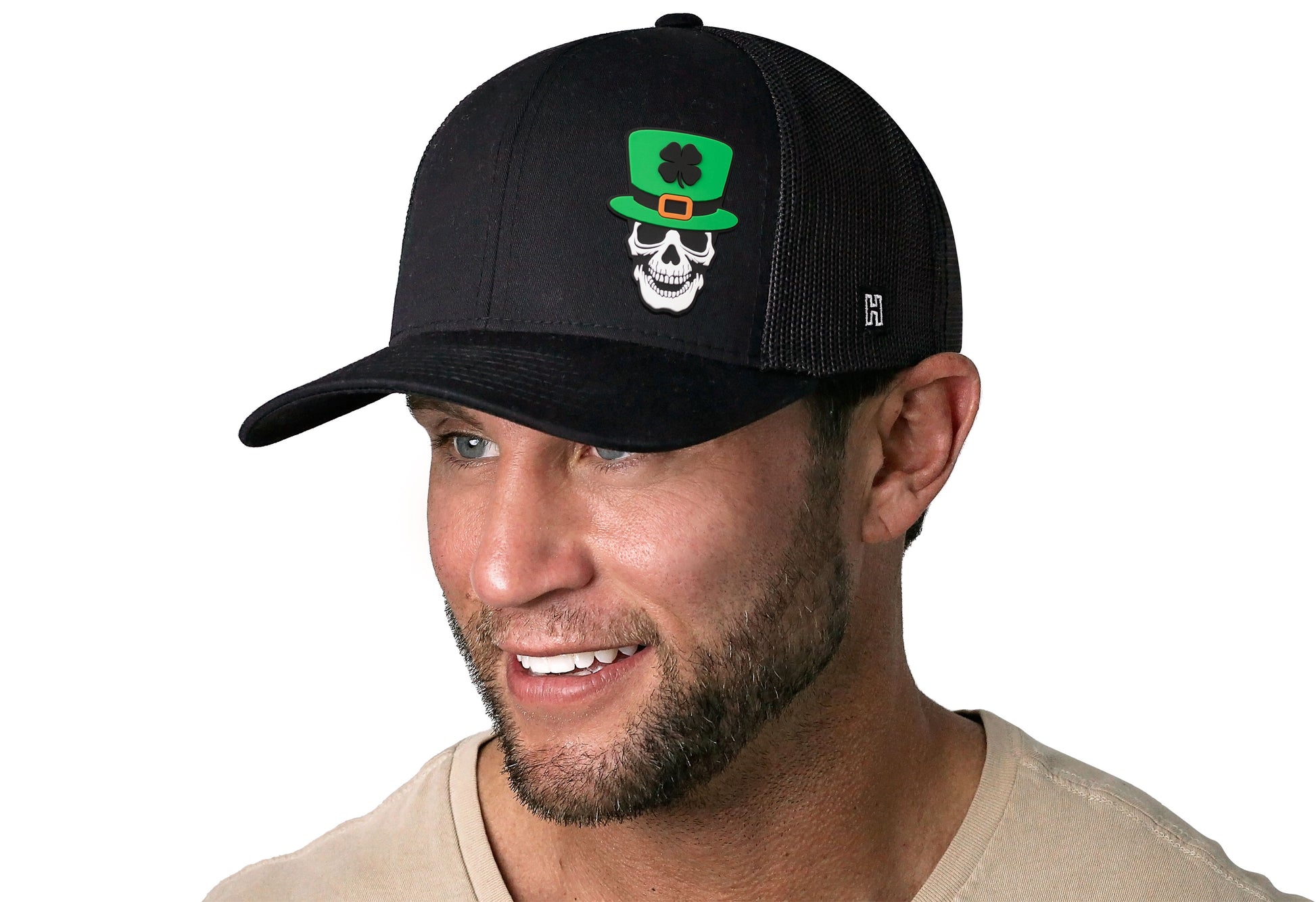 Black trucker hat worn by a male model viewed from the left side and features a Kiss me I'm Irish Puff Embroidered Circle Patch displayed on the front panel. The hat has a classic mesh back design and a curved structured bill