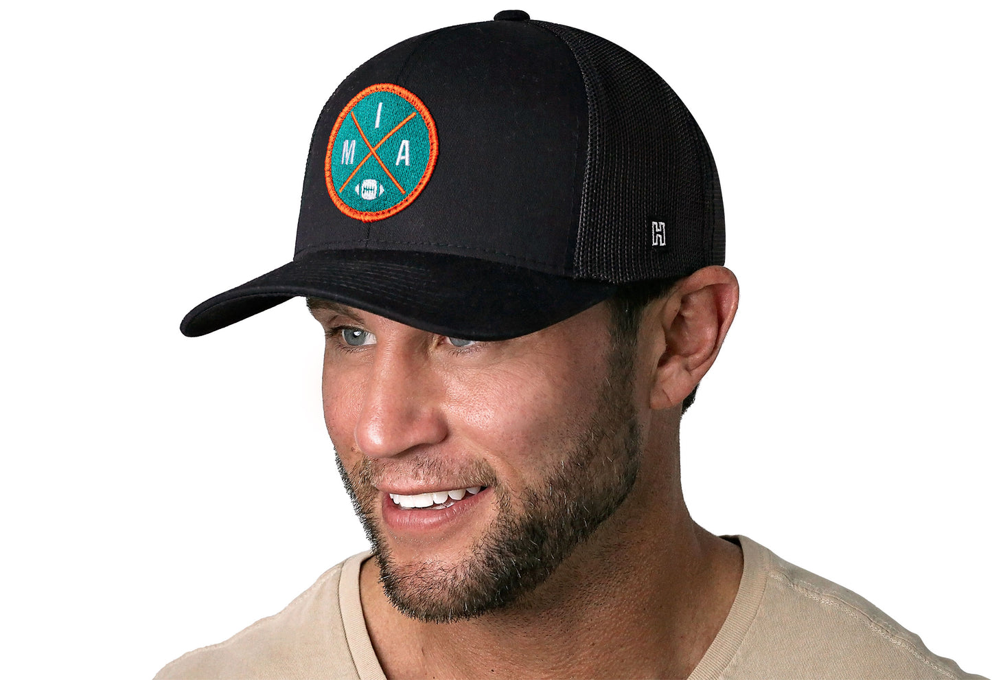 black trucker hat worn by a male model viewed from the left side and features a bold orange and blue embroidered X patch displayed on the front panel. The hat has a classic mesh back design and a curved structured bill