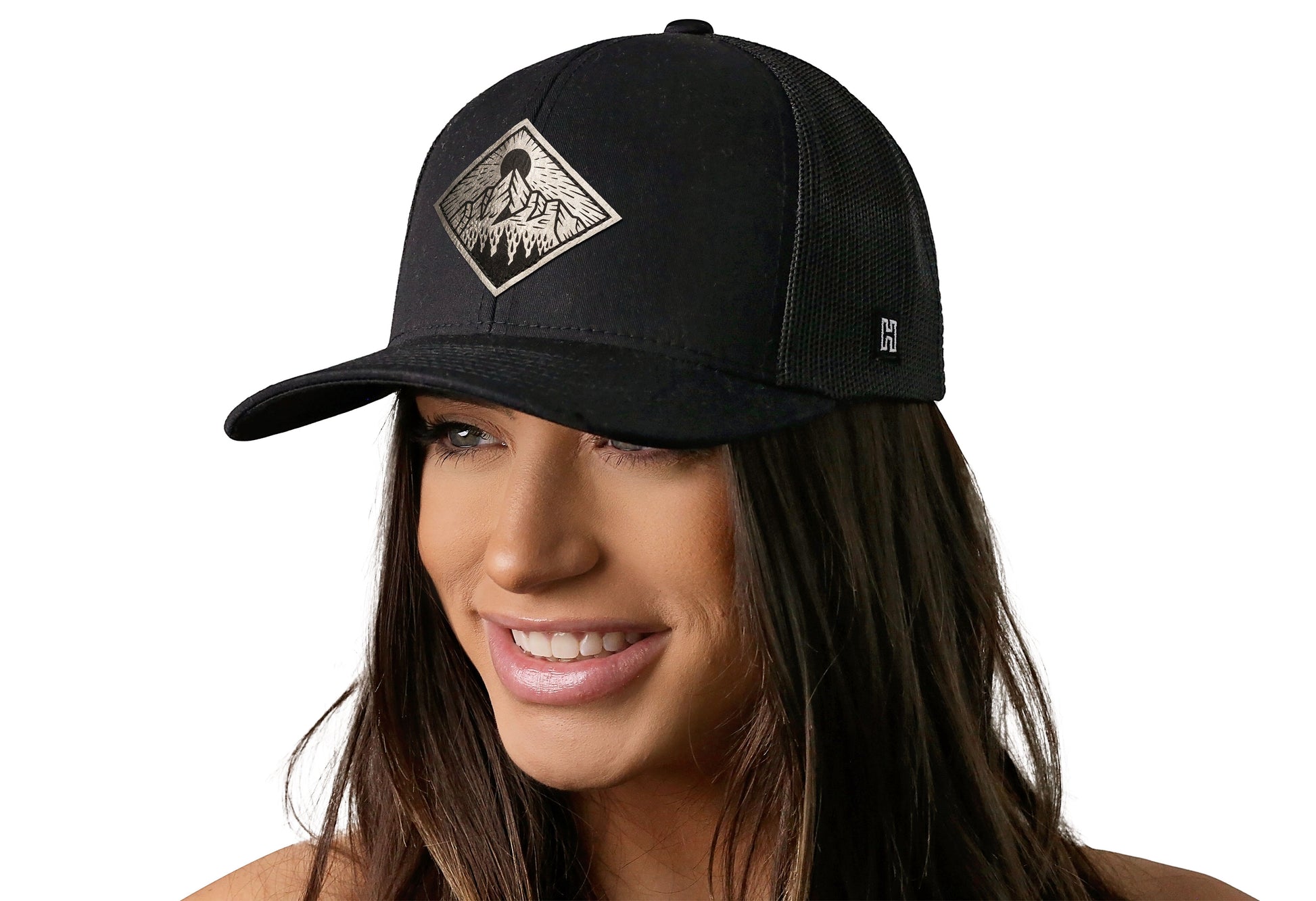 Black trucker hat worn by a female model viewed from the left side and features a Mountains and Trees Silver Faux Leather Black Outdoors Leather (Faux) displayed on the front panel. The hat has a classic mesh back design and a curved structured bill