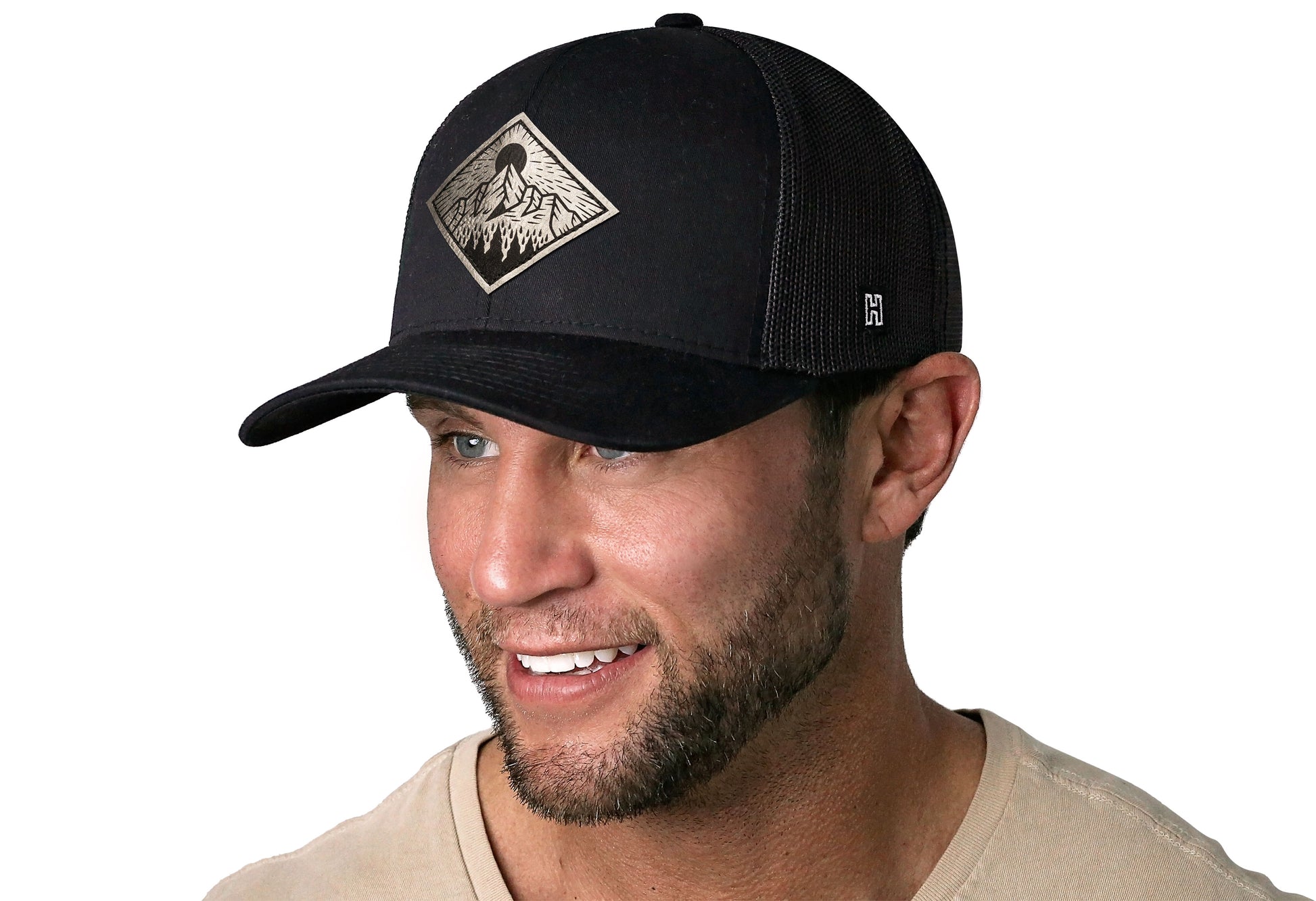 Black trucker hat worn by a male model viewed from the left side and features a Mountains and Trees Silver Faux Leather Black Outdoors Leather (Faux) displayed on the front panel. The hat has a classic mesh back design and a curved structured bill