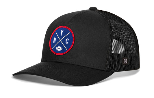 black trucker hat viewed from the right side, showcasing a NYC Football embroidered X patch in blue and red prominently displayed on the front