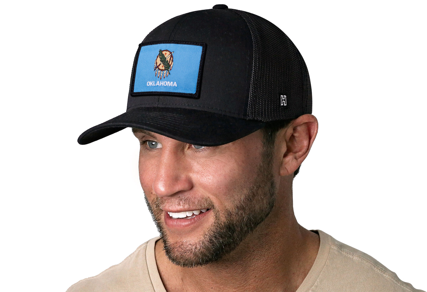 Black trucker hat worn by a male model viewed from the left side and features a Oklahoma Flag Woven Rectangule Patch displayed on the front panel. The hat has a classic mesh back design and a curved structured bill