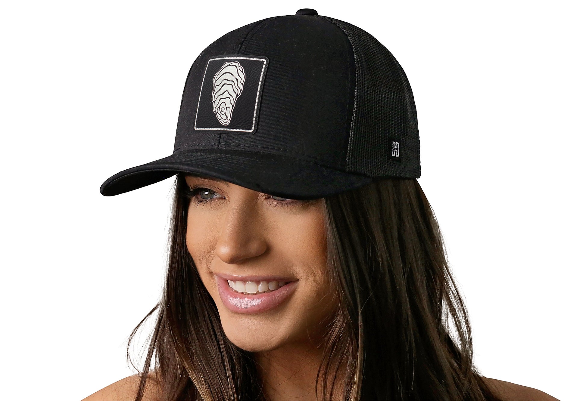 Black trucker hat worn by a female model viewed from the left side and features a Oyster Faux Metallic Leather Rectangle Patch displayed on the front panel. The hat has a classic mesh back design and a curved structured bill