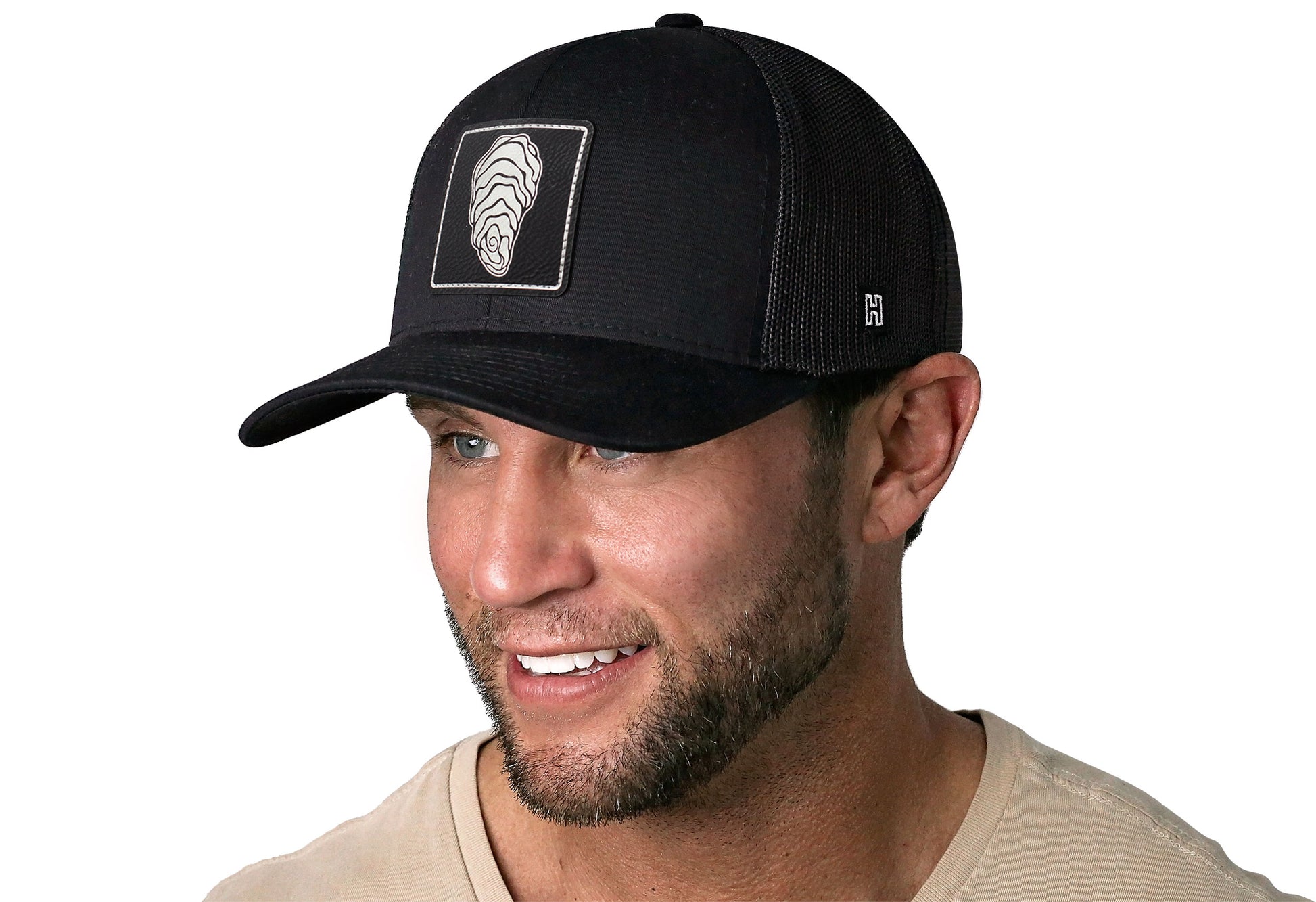 Black trucker hat worn by a male model viewed from the left side and features a Oyster Faux Metallic Leather Rectangle Patch displayed on the front panel. The hat has a classic mesh back design and a curved structured bill