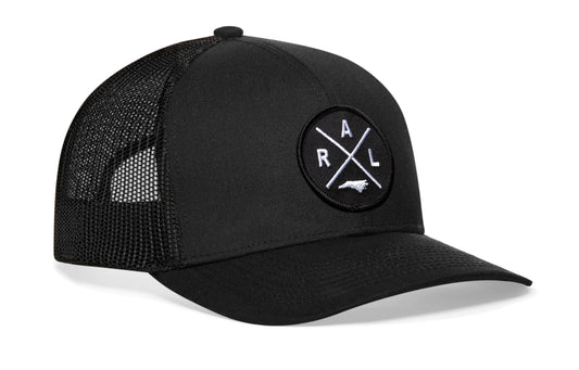 Black trucker hat viewed from the right side, showcasing a Raleigh RAL X Embroidered Circle Patch prominently displayed on the front