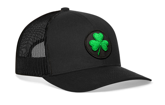 Black trucker hat viewed from the right side, showcasing a Shamrock Black St Patrick's Day Embroidered Patch prominently displayed on the front