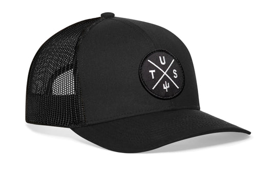 Black trucker hat viewed from the right side, showcasing a Tucson TUS X Embroidered Black Circle Patch prominently displayed on the front