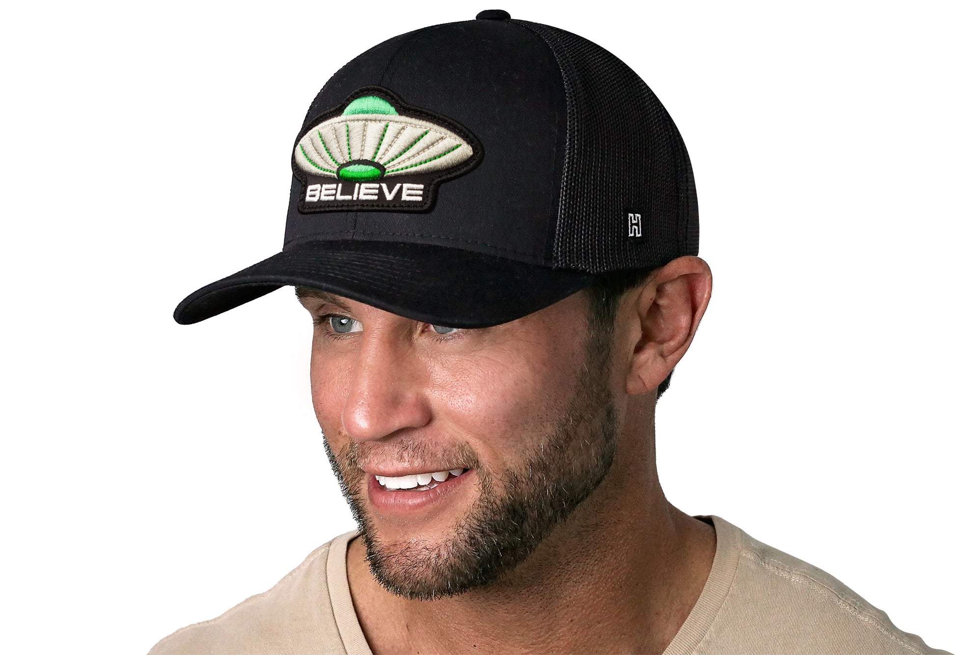 black trucker hat worn by a male model viewed from the left side and features a UFO 'Believe' Puff Embroidery Patch 3D Embroidery Cut-To-Shape Patch displayed on the front panel. The hat has a classic mesh back design and a curved structured bill
