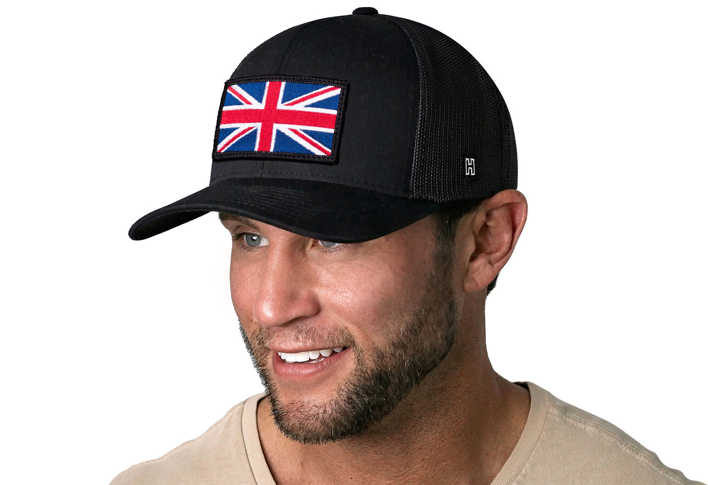 Black trucker hat worn by a male model viewed from the left side and features a United Kingdom Flag Embroidered Rectangle Patch displayed on the front panel. The hat has a classic mesh back design and a curved structured bill