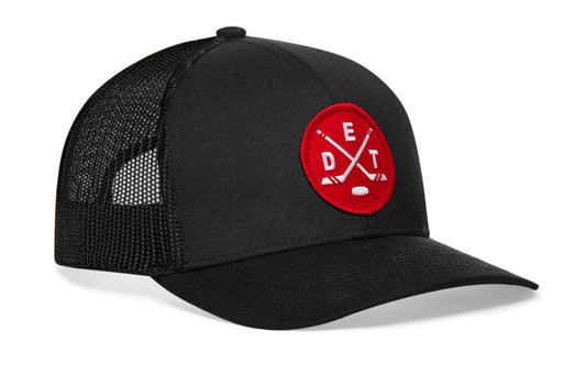 black trucker hat viewed from the right side, showcasing a red and white hockey embroidered X patch prominently displayed on the front