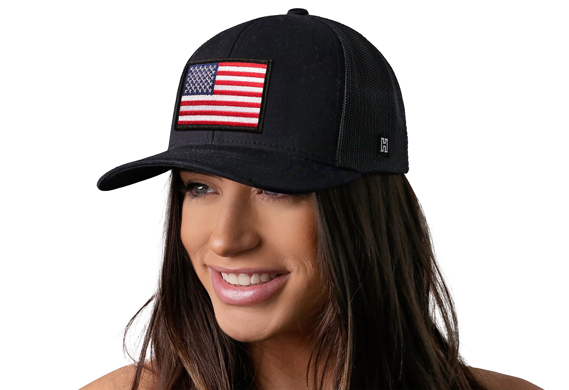 black trucker hat worn by a female model viewed from the left side and features a American Flag Embroidered Rectangle Patch displayed on the front panel. The hat has a classic mesh back design and a curved structured bill