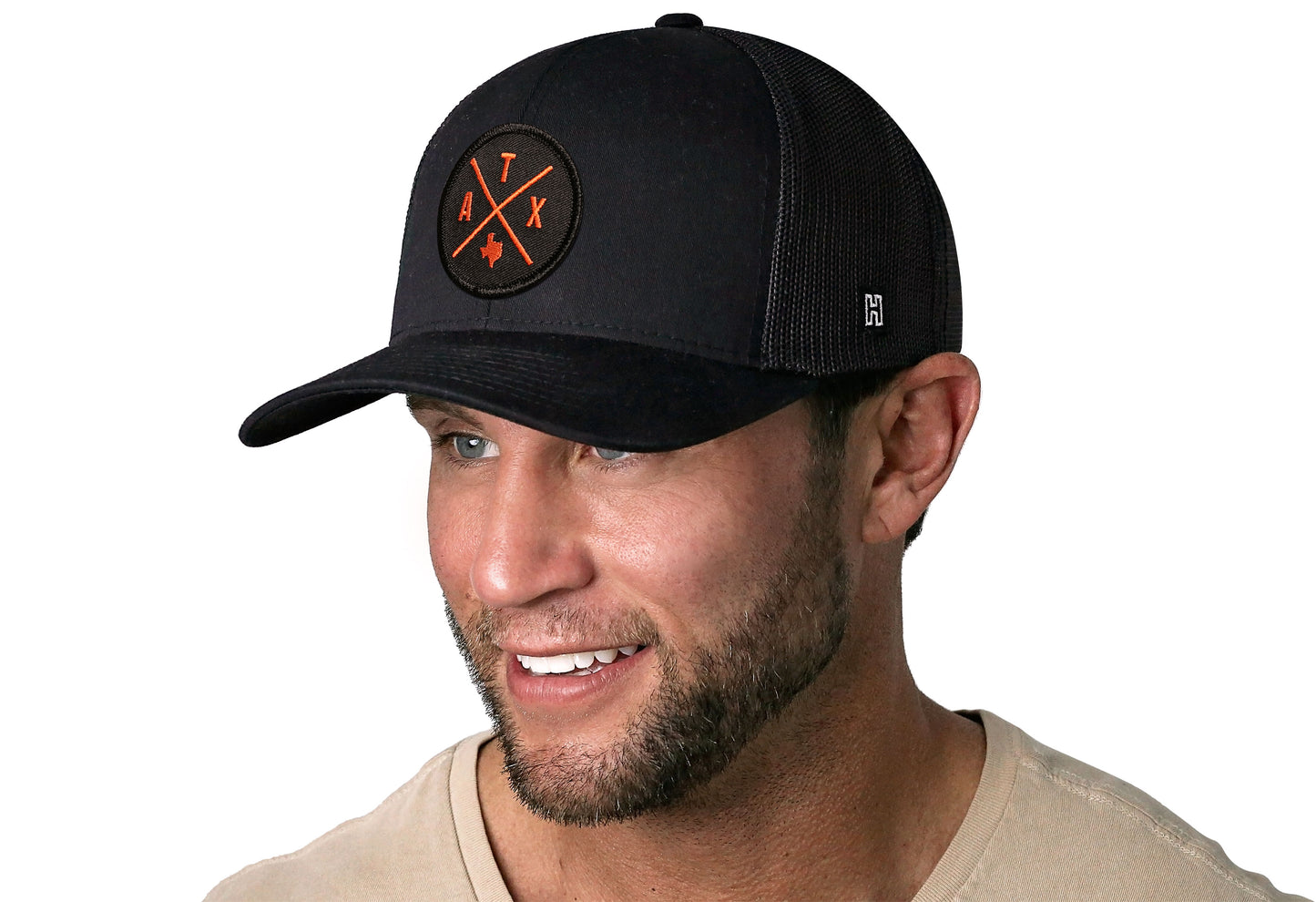 Black trucker hat worn by a male model viewed from the left side and features a Austin (Orange) ATX Embroidered X Patch displayed on the front panel. The hat has a classic mesh back design and a curved structured bill
