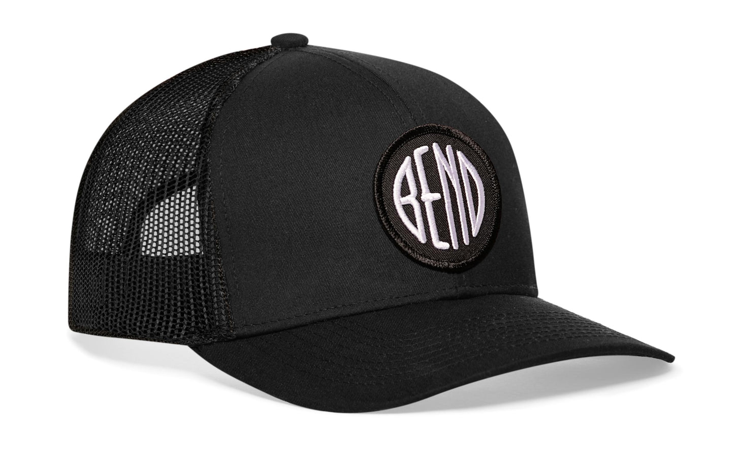 Black trucker hat viewed from the right side, showcasing a Bend Embroidered Circle Patch prominently displayed on the front