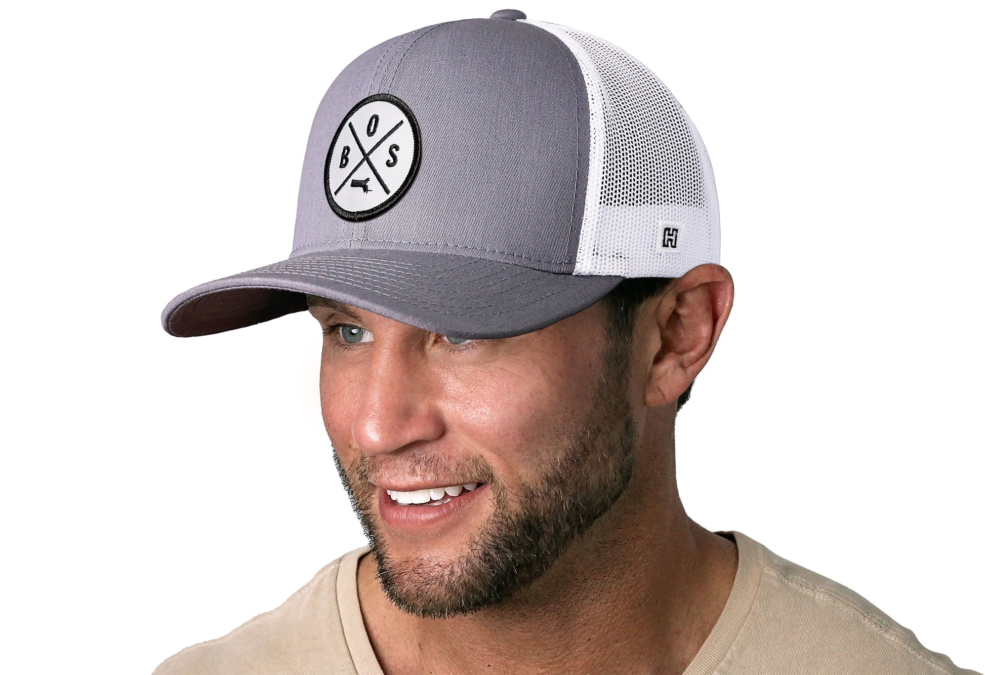 Gray-White trucker hat worn by a male model viewed from the left side and features a Boston BOS X Embroidered White Circle Patch displayed on the front panel. The hat has a classic mesh back design and a curved structured bill