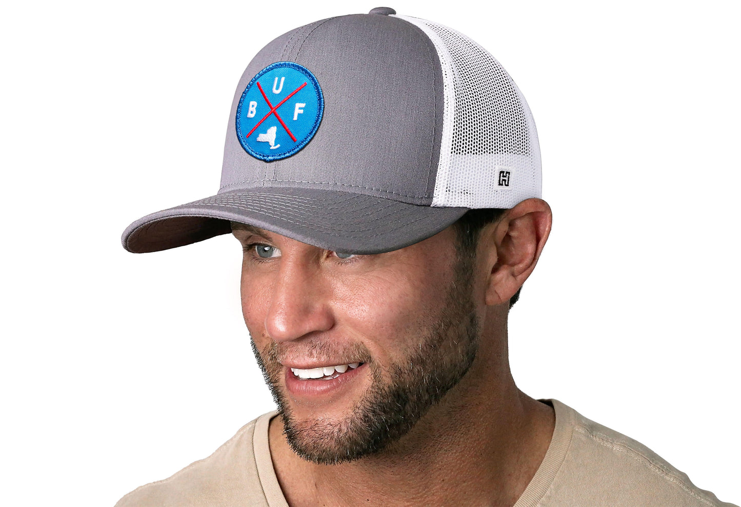 Gray-White trucker hat worn by a male model viewed from the left side and features a Buffalo BUF X Red, White, Blue Embroidered Circle Patch displayed on the front panel. The hat has a classic mesh back design and a curved structured bill