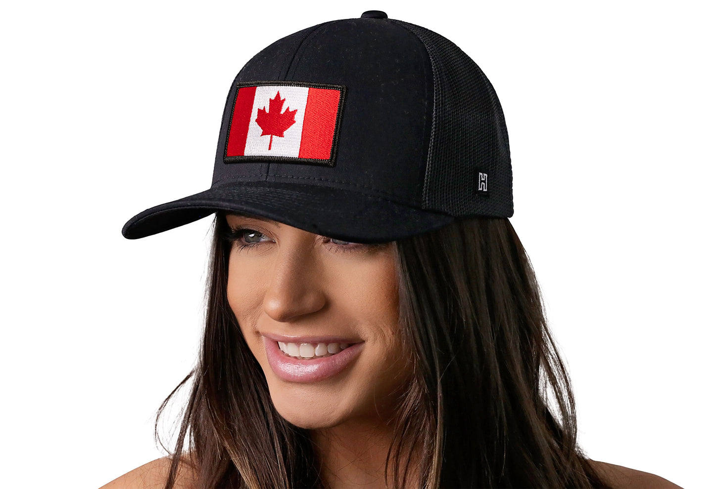 Black trucker hat worn by a female model viewed from the left side and features a Canadian Flag Embroidered Rectangle Patch displayed on the front panel. The hat has a classic mesh back design and a curved structured bill