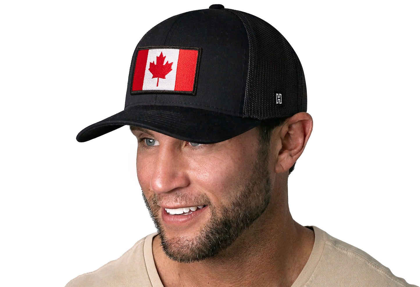 Black trucker hat worn by a male model viewed from the left side and features a Canadian Flag Embroidered Rectangle Patch displayed on the front panel. The hat has a classic mesh back design and a curved structured bill