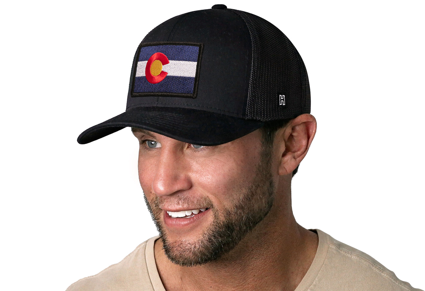 Black trucker hat worn by a male model viewed from the left side and features a Colorado Flag Embroidered Rectangle Patch displayed on the front panel. The hat has a classic mesh back design and a curved structured bill
