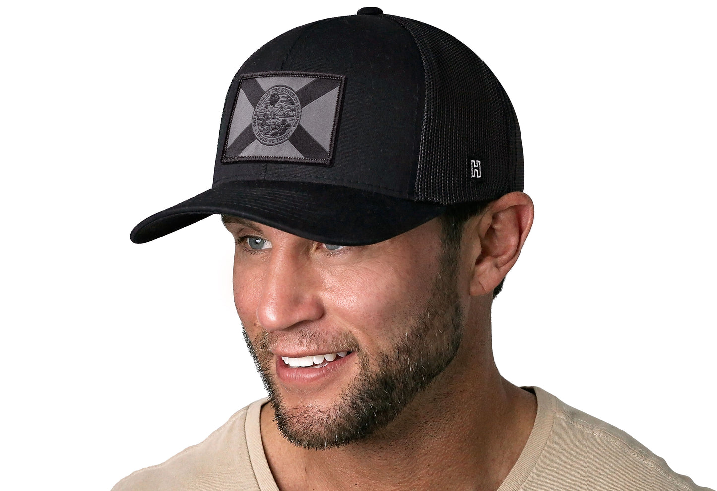 Black trucker hat worn by a male model viewed from the left side and features a Florida Flag Woven Tactical Retangle Patch displayed on the front panel. The hat has a classic mesh back design and a curved structured bill