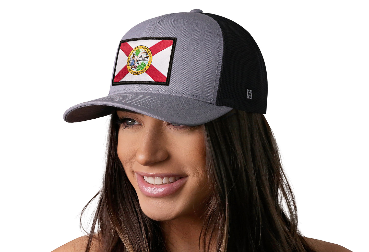 Gray-Black trucker hat worn by a female model viewed from the left side and features a Florida Flag Woven Retangle Patch displayed on the front panel. The hat has a classic mesh back design and a curved structured bill