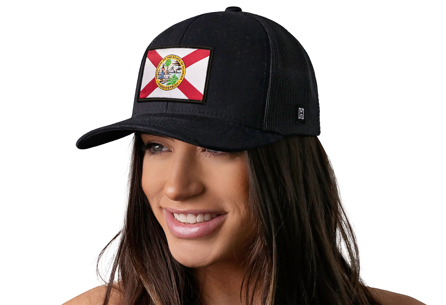 Black trucker hat worn by a female model viewed from the left side and features a Florida Flag Woven Retangle Patch displayed on the front panel. The hat has a classic mesh back design and a curved structured bill