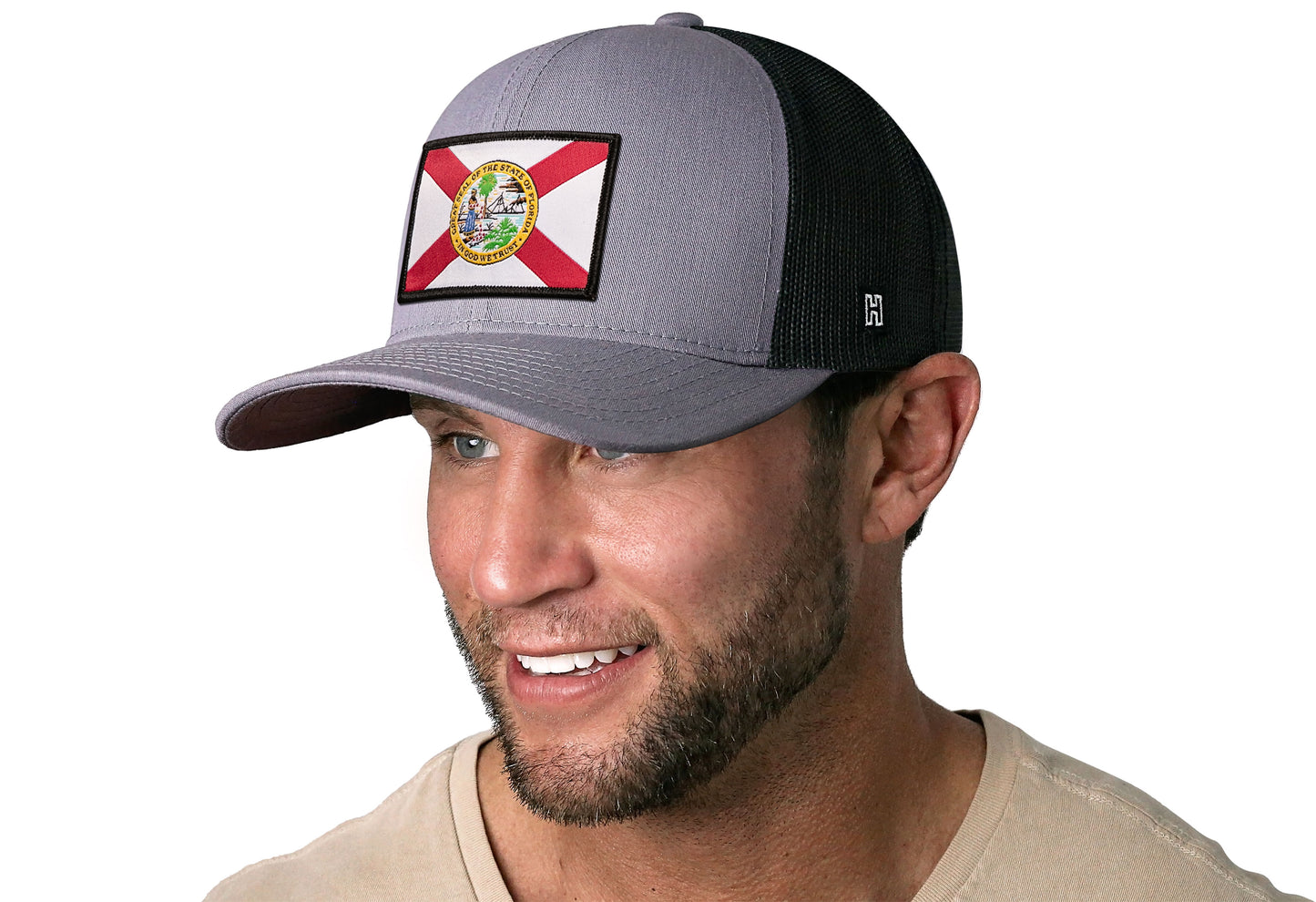 Gray-Black trucker hat worn by a male model viewed from the left side and features a Florida Flag Woven Retangle Patch displayed on the front panel. The hat has a classic mesh back design and a curved structured bill
