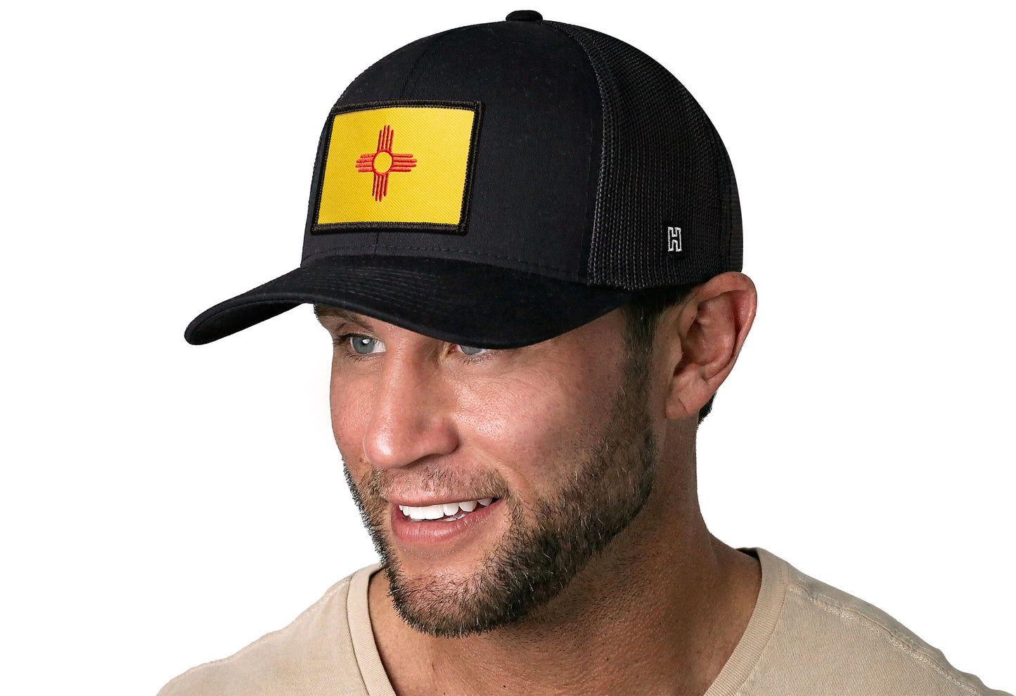 Black trucker hat worn by a male model viewed from the left side and features a New Mexico Woven Rectangle Patch displayed on the front panel. The hat has a classic mesh back design and a curved structured bill