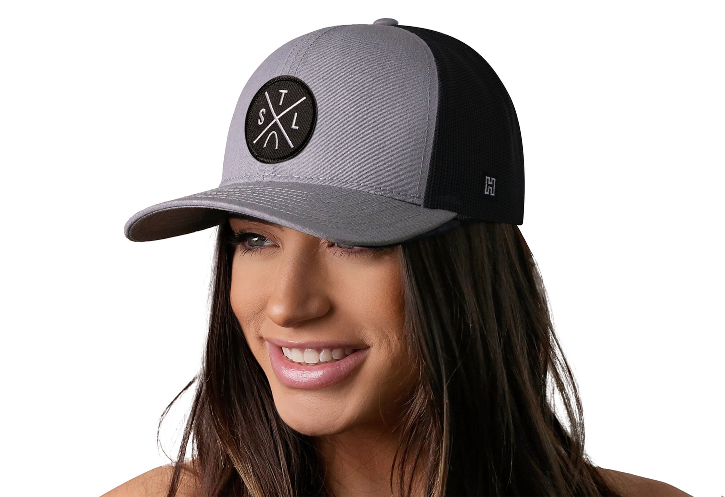 Gray-Black trucker hat worn by a female model viewed from the left side and features a St Louis STL X Embroidered Circle Patch displayed on the front panel. The hat has a classic mesh back design and a curved structured bill