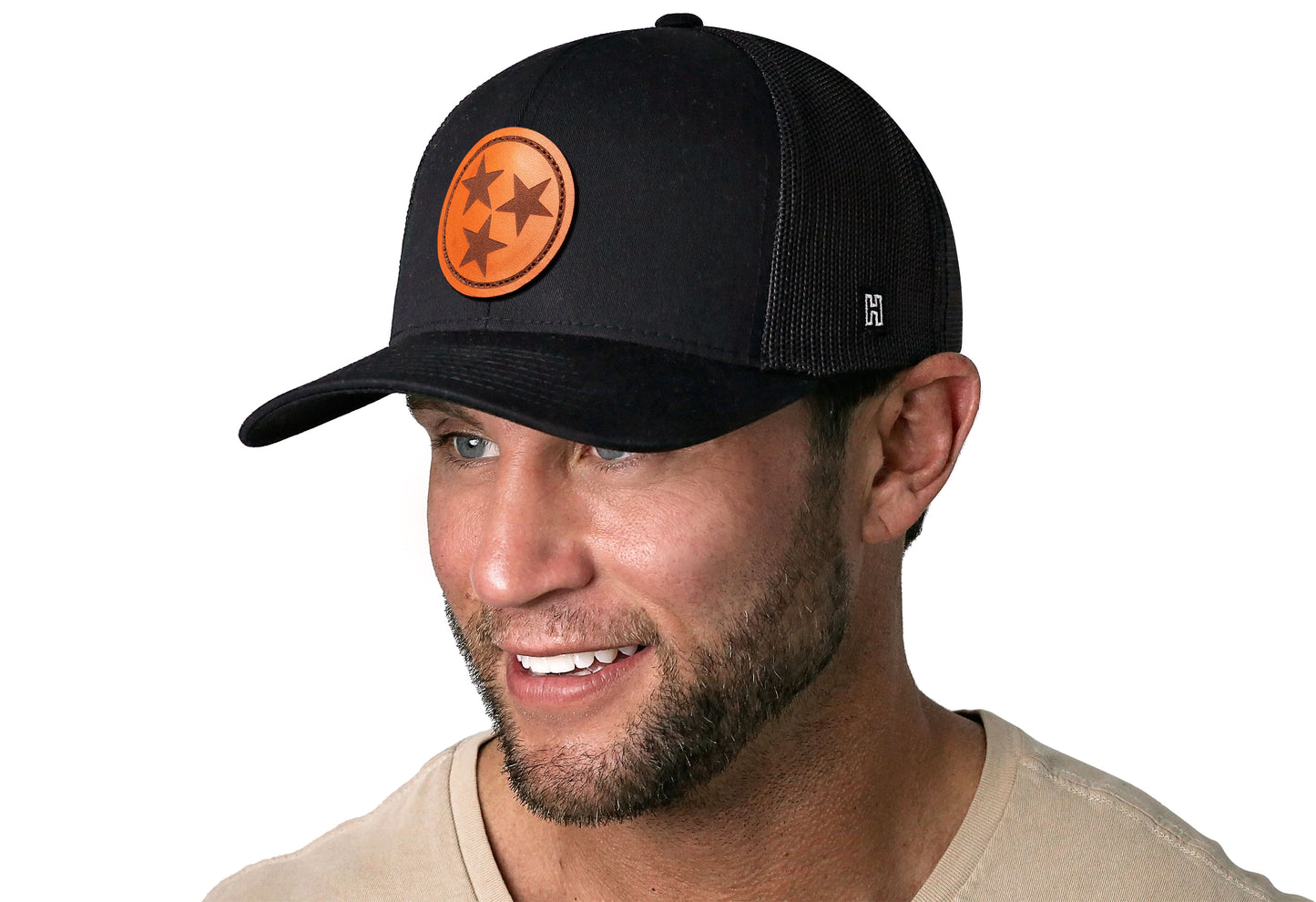 Black trucker hat worn by a male model viewed from the left side and features a Tennessee Leather TN Leather displayed on the front panel. The hat has a classic mesh back design and a curved structured bill