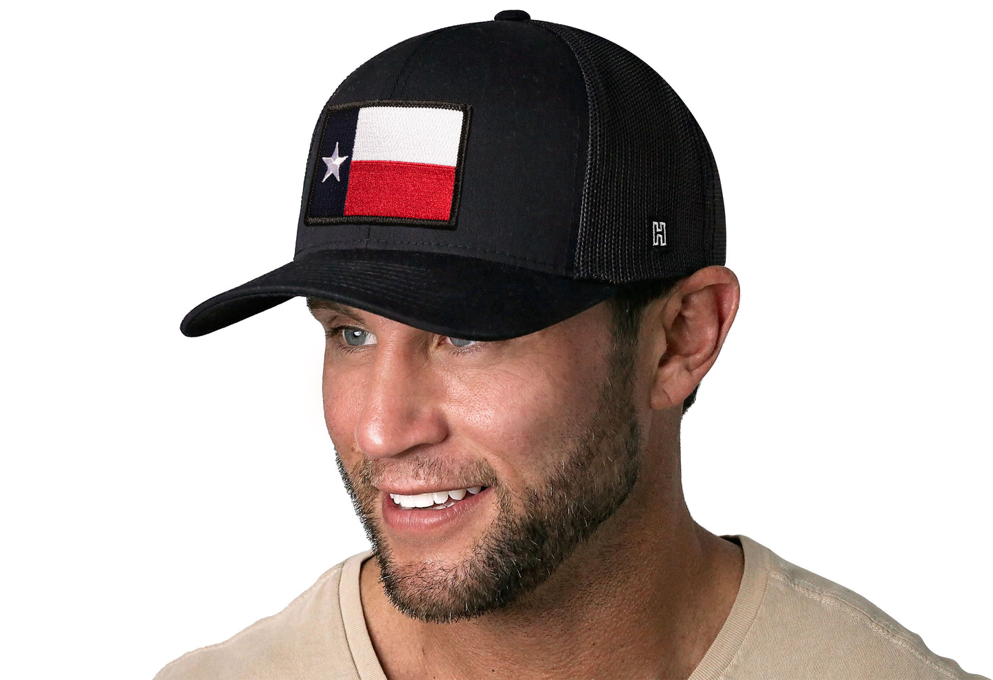 Black trucker hat worn by a male model viewed from the left side and features a Texas TX Embroidered Flag Patch displayed on the front panel. The hat has a classic mesh back design and a curved structured bill